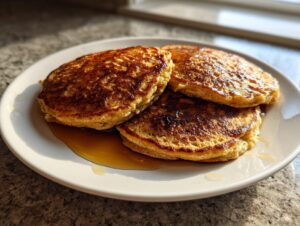 Three golden brown banana pancakes stacked on a white plate, drizzled with syrup.