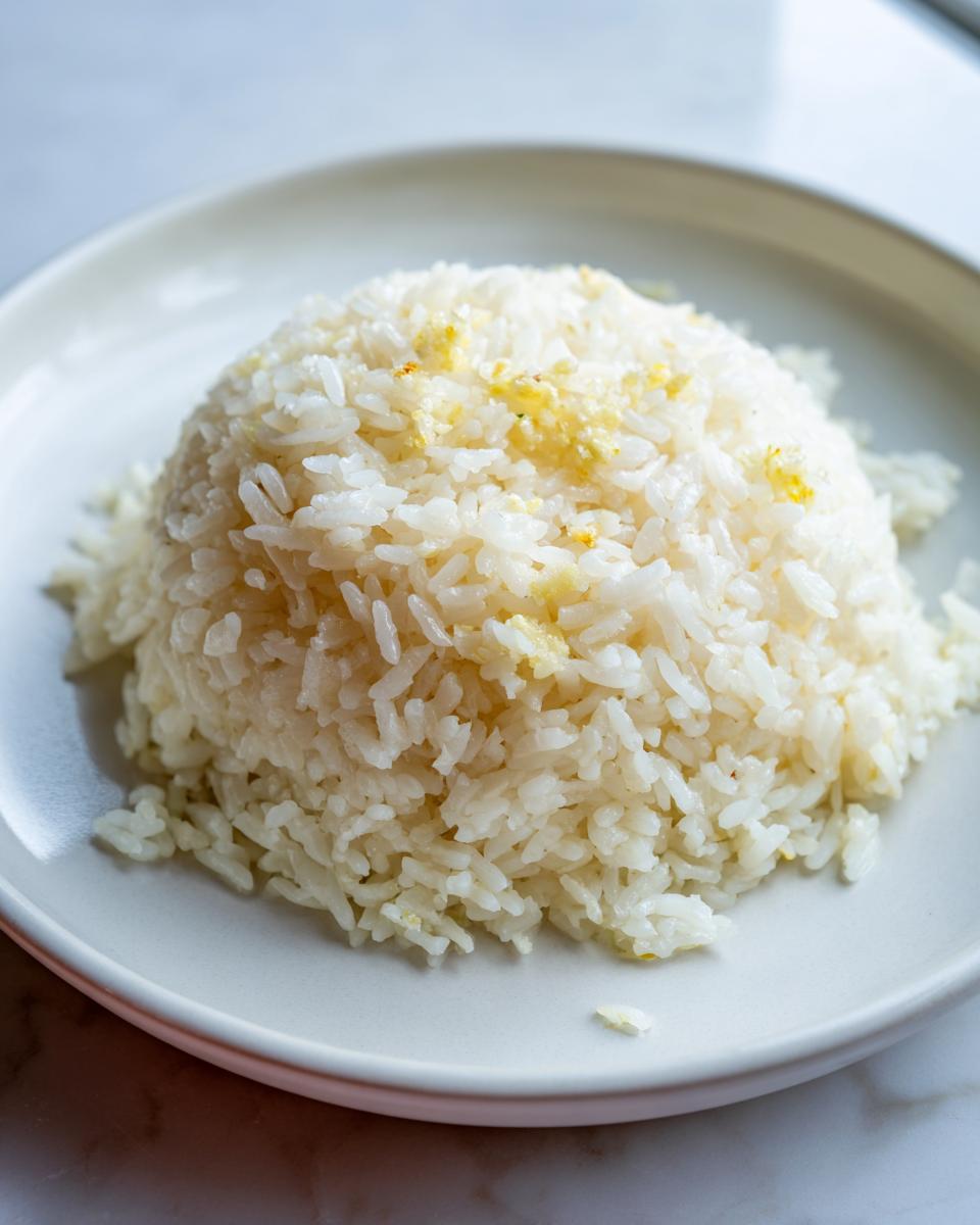A perfectly molded mound of fluffy white butter rice topped with melted butter, served on a light gray plate.