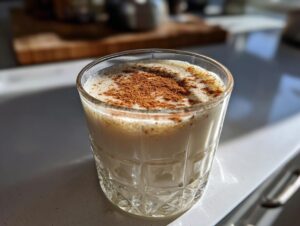 A glass of creamy, frothy coquito recipe topped generously with ground cinnamon.