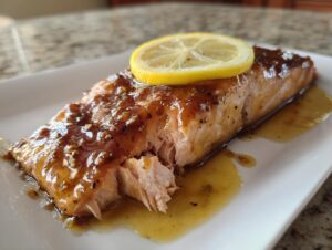 Close-up of a perfectly cooked salmon fillet with a shiny, sweet glaze and a lemon slice on top.