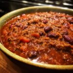 Close-up of a rich, steaming bowl filled with the best chili recipe, featuring ground meat and dark red kidney beans.