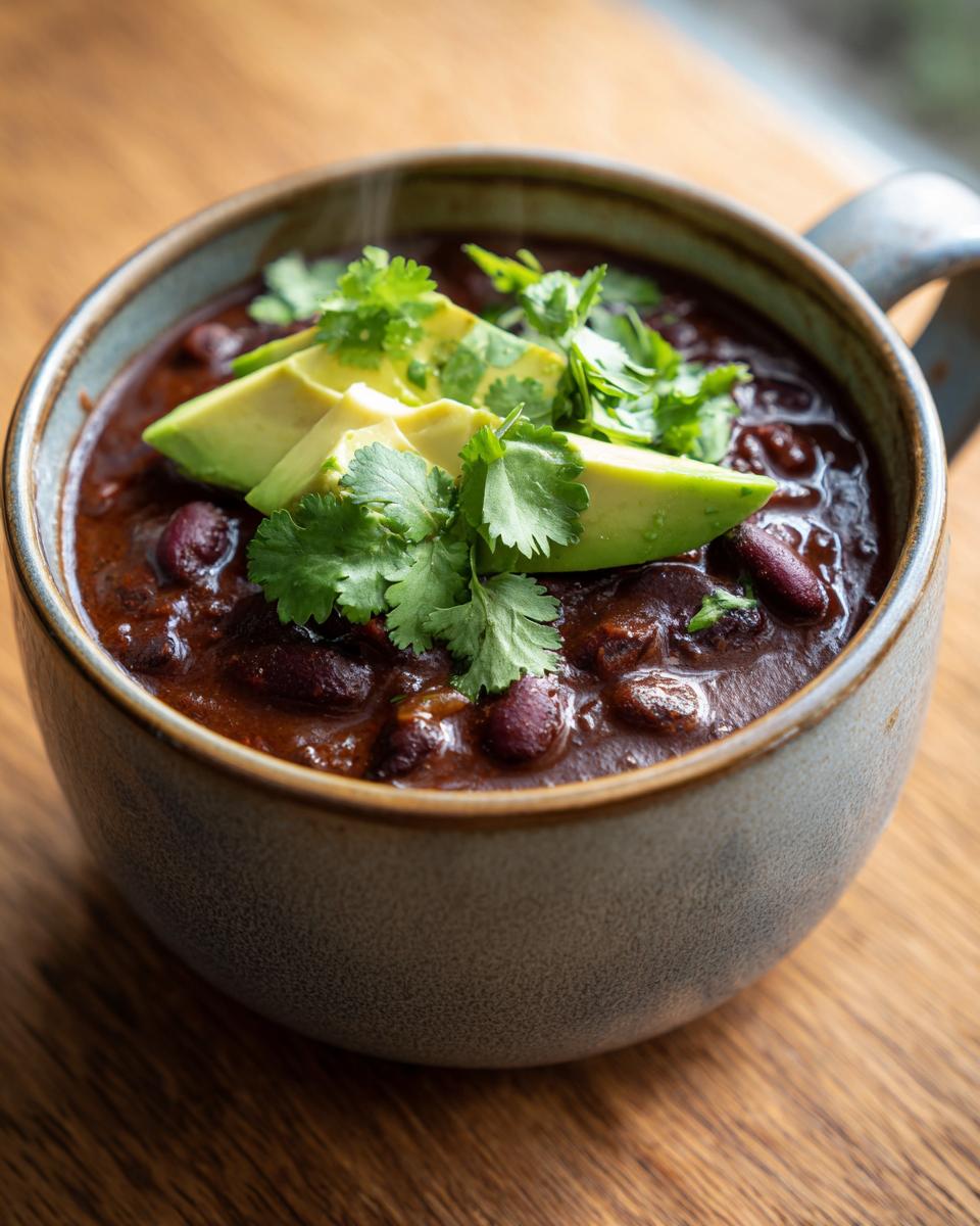 Close-up of a steaming bowl of hearty black bean soup topped with sliced avocado and fresh cilantro.