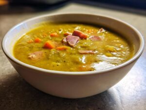 Close-up of a creamy, thick bowl of homemade pea soup topped with diced ham and carrots.
