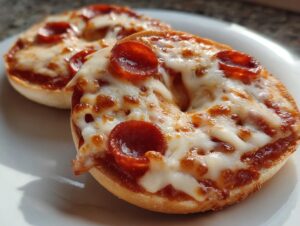 Two freshly baked pepperoni pizza bagels topped with melted mozzarella cheese on a white plate.