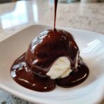 A scoop of vanilla ice cream being drenched with thick, glossy homemade chocolate sauce recipe.