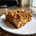 A square slice of baked oatmeal with a thick, crunchy oat crumble topping, served on a white plate.