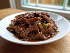 A close-up of tender, shredded Mississippi pot roast served in a white bowl with visible pepperoncini slices and rich gravy.