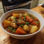 A close-up of a hearty slow cooker chicken stew filled with tender chicken, carrots, potatoes, and peas in a rich broth.