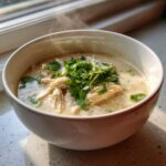 Close-up of a steaming white bowl filled with creamy chicken chili recipe, topped with fresh cilantro.