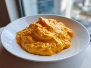 A close-up of thick, bright orange nacho cheese sauce mounded in a white bowl near a window.