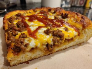 Close-up of a thick slice of taco pizza showing seasoned ground beef, melted cheddar and mozzarella cheese, and a drizzle of sauce.
