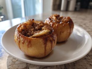 Two perfectly cooked baked apples, stuffed with a cinnamon and brown sugar filling, sitting on a white plate.