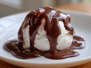 A scoop of vanilla ice cream generously covered in rich, glossy chocolate sauce recipe topping.