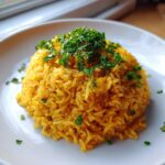 A mound of bright yellow turmeric rice garnished generously with fresh chopped parsley on a white plate.