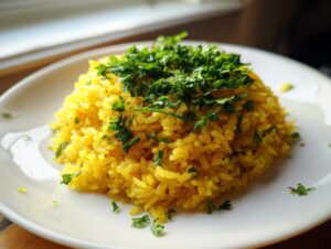 A mound of bright yellow turmeric rice garnished generously with fresh chopped parsley on a white plate.