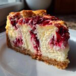 A close-up slice of rich white chocolate raspberry cheesecake showing the creamy filling and graham cracker crust.