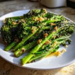 A plate of bright green, sautéed broccolini topped with toasted garlic breadcrumbs.