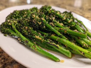 Close-up of bright green, tender broccolini stalks seasoned with crispy garlic bits on a white plate.