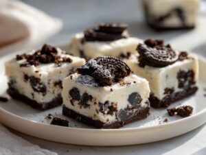 Four squares of creamy white Oreo fudge loaded with dark chocolate cookie pieces, topped with Oreo halves.