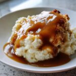 Close-up of mashed potatoes topped with fried chicken and rich chicken gravy.