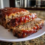 Close-up of a freshly baked meatloaf, sliced to show the texture, covered in a thick, glossy ketchup glaze.