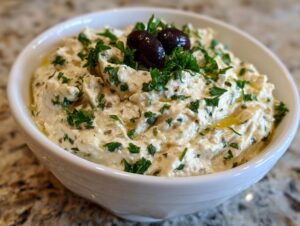 Close-up of a creamy, white olive dip garnished with fresh parsley and two Kalamata olives.