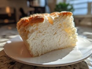 A fluffy, white slice of angel food cake with a golden-brown crust sitting on a white plate.