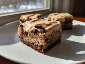 A square slice of banana bread brownies topped with peanut butter frosting and chocolate chips sits on a white plate.