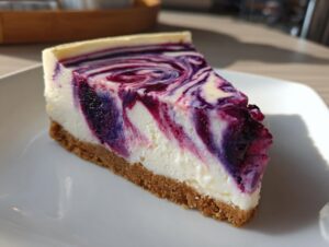 A perfect slice of blueberry cheesecake featuring a graham cracker crust and a creamy top swirled with deep purple blueberry sauce.
