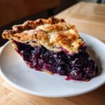 A generous slice of homemade blueberry pie recipe showing a thick, juicy blueberry filling and flaky golden crust.