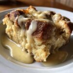 Close-up of a warm slice of bread pudding recipe generously topped with creamy vanilla sauce.