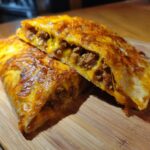 Close-up of cheesy pocket tacos cut in half, revealing melted cheese and seasoned ground beef filling.