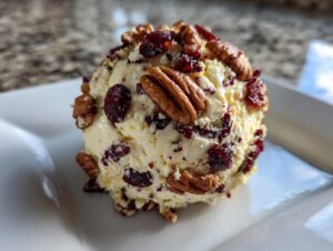 A close-up, featured image of a perfectly formed cranberry pecan cheese ball coated in nuts and dried fruit.
