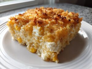 A square slice of rich cream cheese corn casserole featuring visible corn kernels and a golden, crispy breadcrumb topping.