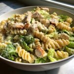 Close-up of creamy chicken caesar pasta salad featuring rotini pasta, grilled chicken pieces, and romaine lettuce.