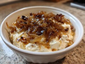 Close-up of creamy white onion dip topped generously with deeply caramelized onions.