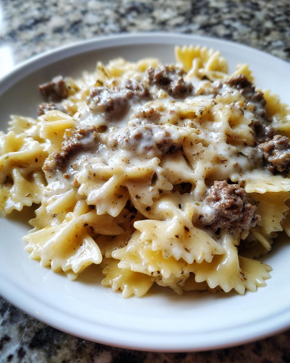 Close-up of creamy parmesan garlic beef bowtie pasta coated in a rich white sauce and served in a white bowl.