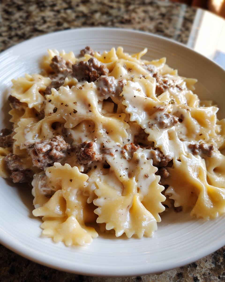 Close-up of creamy parmesan garlic beef bowtie pasta coated in a rich white sauce and topped with cracked black pepper.