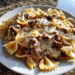 Close-up of creamy parmesan garlic beef bowtie pasta topped with melted cheese on a white plate.
