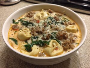 Close-up of a hearty bowl of creamy sausage tortellini soup with spinach and melted cheese.