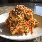 A mound of creamy thai chicken salad mixed with shredded carrots and topped with chopped peanuts on a white plate.