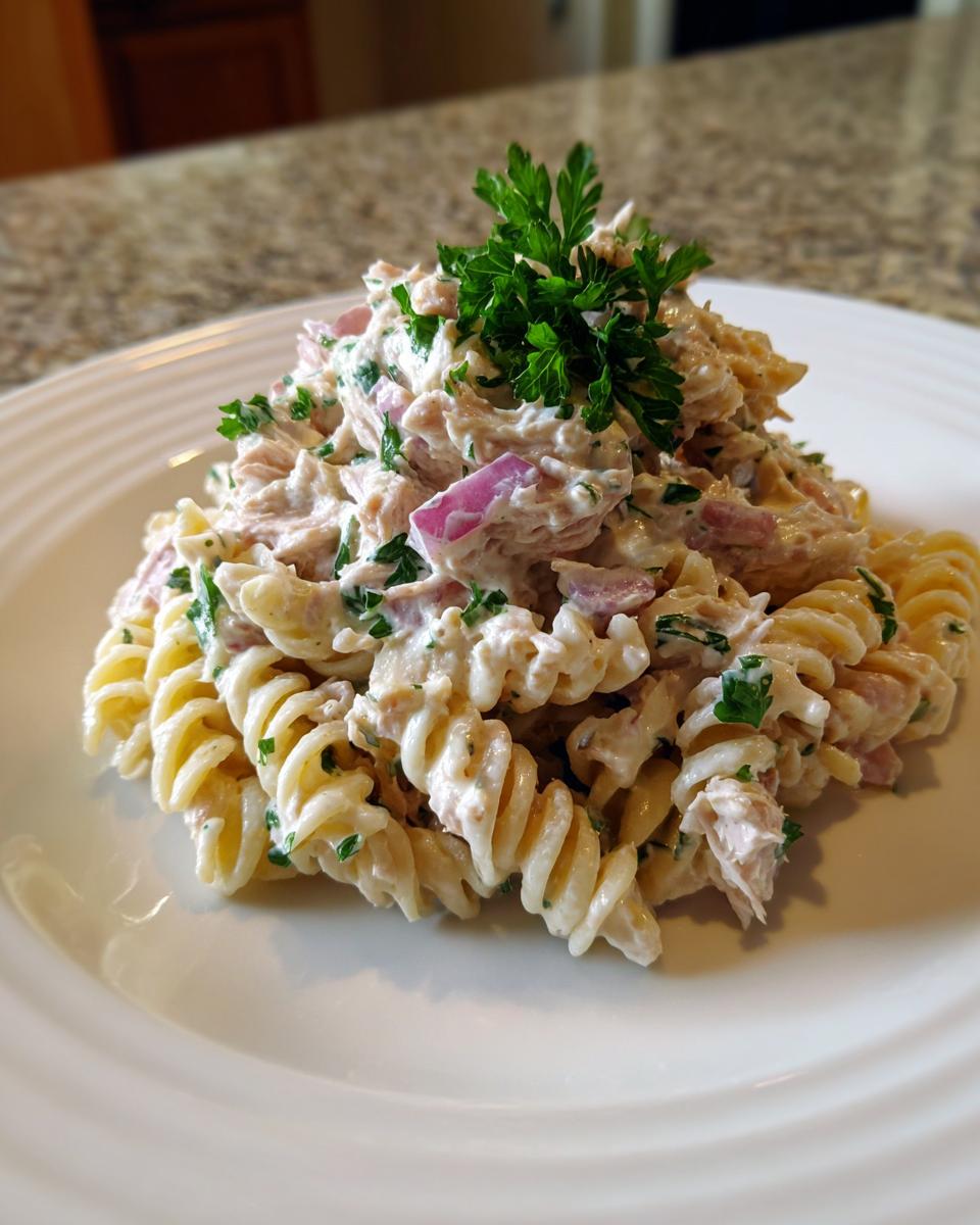 A mound of creamy tuna pasta salad made with rotini pasta, red onion, and topped with fresh parsley.