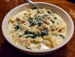 Close-up of a white bowl filled with creamy white chicken lasagna soup, featuring pasta, chicken chunks, and spinach.