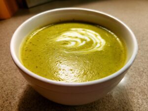 A close-up of a bowl of creamy, vibrant green zucchini soup topped with a swirl of white cream.