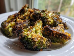Close-up of perfectly crispy, roasted smashed broccoli florets with a browned, seasoned crust served on a white plate.