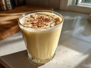 A glass of thick, creamy homemade eggnog topped generously with ground cinnamon.