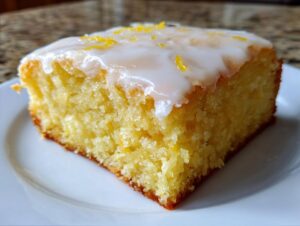 A close-up of a single slice of fudgy lemon brownies topped with white glaze and lemon zest.
