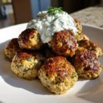 A pile of perfectly browned greek chicken meatballs topped with a dollop of creamy tzatziki sauce and fresh dill.