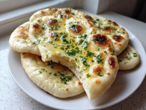A stack of freshly made homemade naan bread brushed with melted butter and topped with chopped parsley.