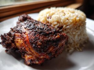 Close-up of a piece of dark, spicy Jamaican jerk chicken served next to a mound of rice and peas.